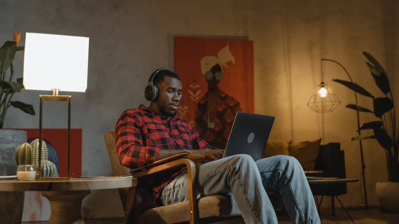 Homem negro em casa usando notebook e fone de ouvido.