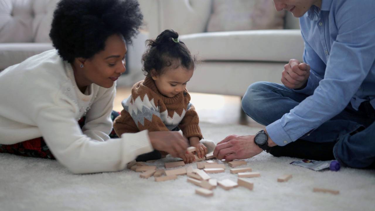 Um homem e uma mulher aparecem brincando com um bebê.