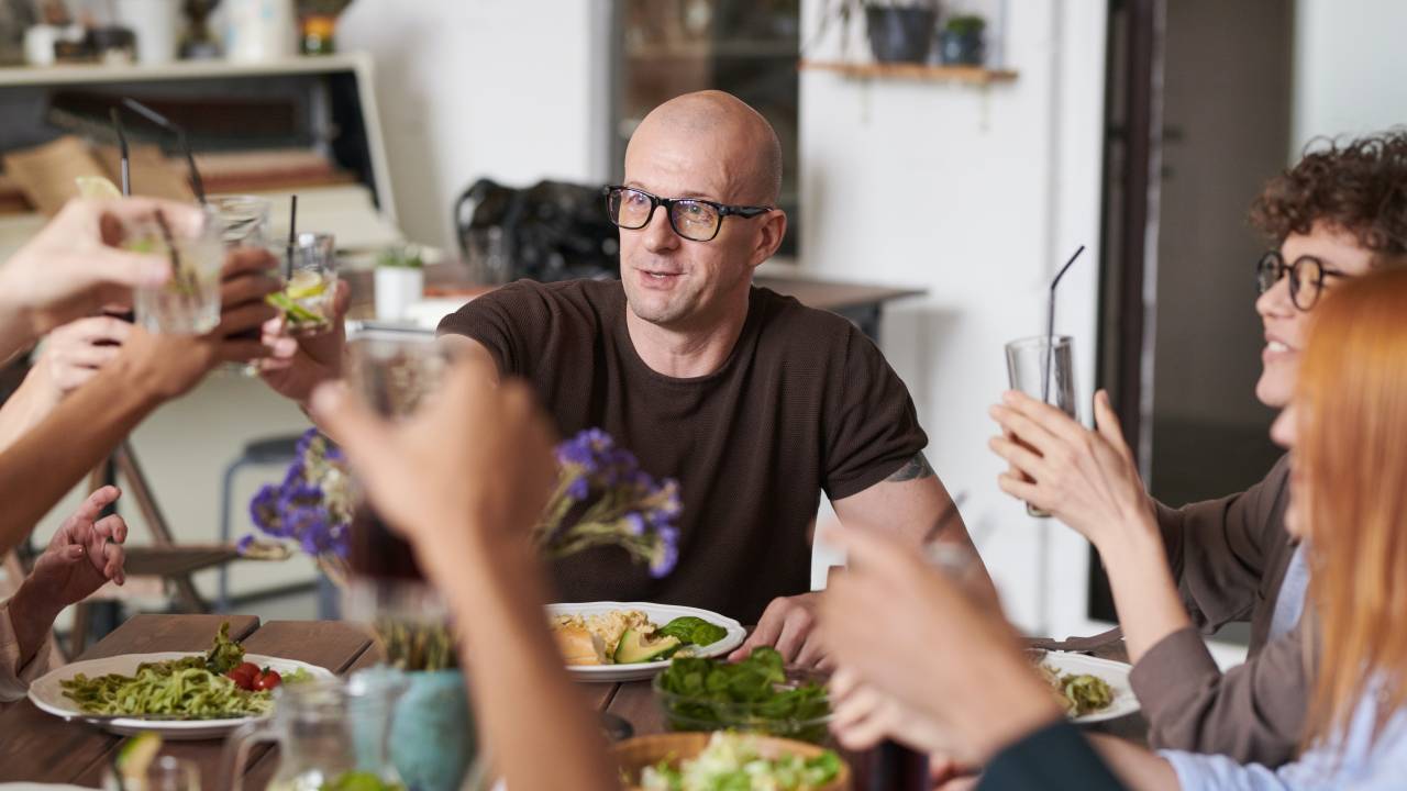 Pessoas ao redor da mesa, comendo e fazendo um brinde