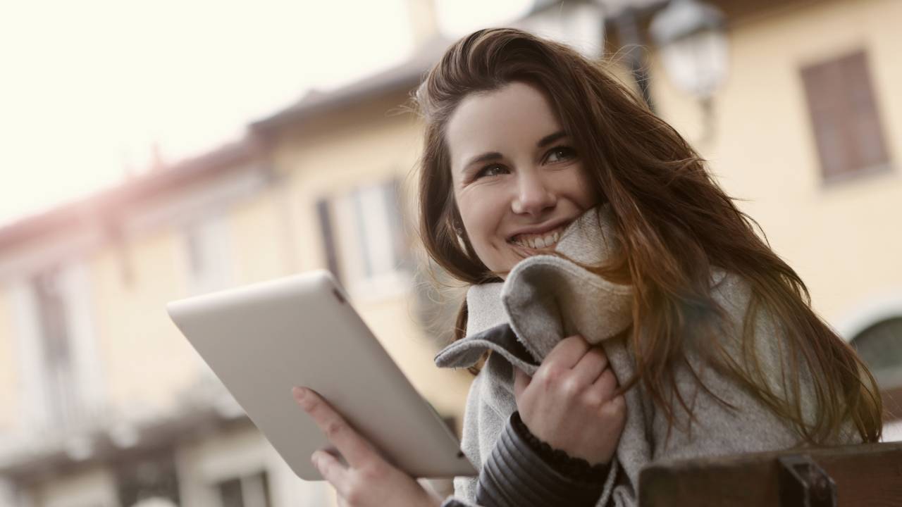 Mulher de cabelo liso comprido segura um tablet e sorri