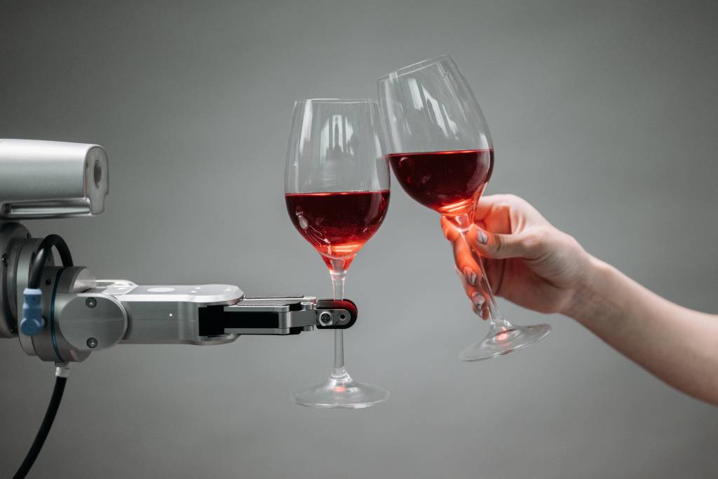 Um robô segura uma taça de vinho e faz um brinde com um ser humano, que segura uma segunda taça.