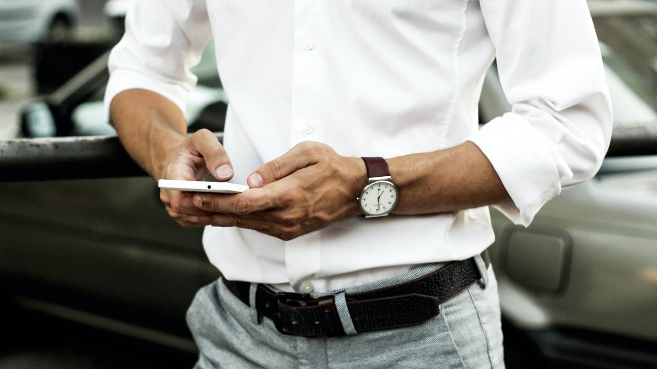 Executivo de camisa branca, jeans e cinto acessa smartphone