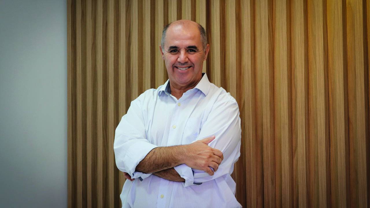 André está vestido com uma camisa branca e está de braços cruzados