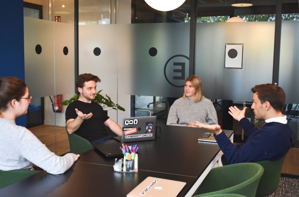 Grupo de quatro pessoas conversa em uma sala de reuniões em uma empresa