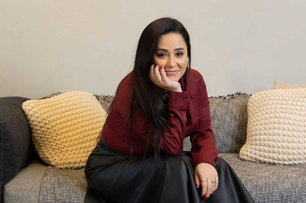 Foto de Raíssa Mendes, diretora de RH da WeWork. Ela está sentada em um sofá e sorri em direção à câmera.
