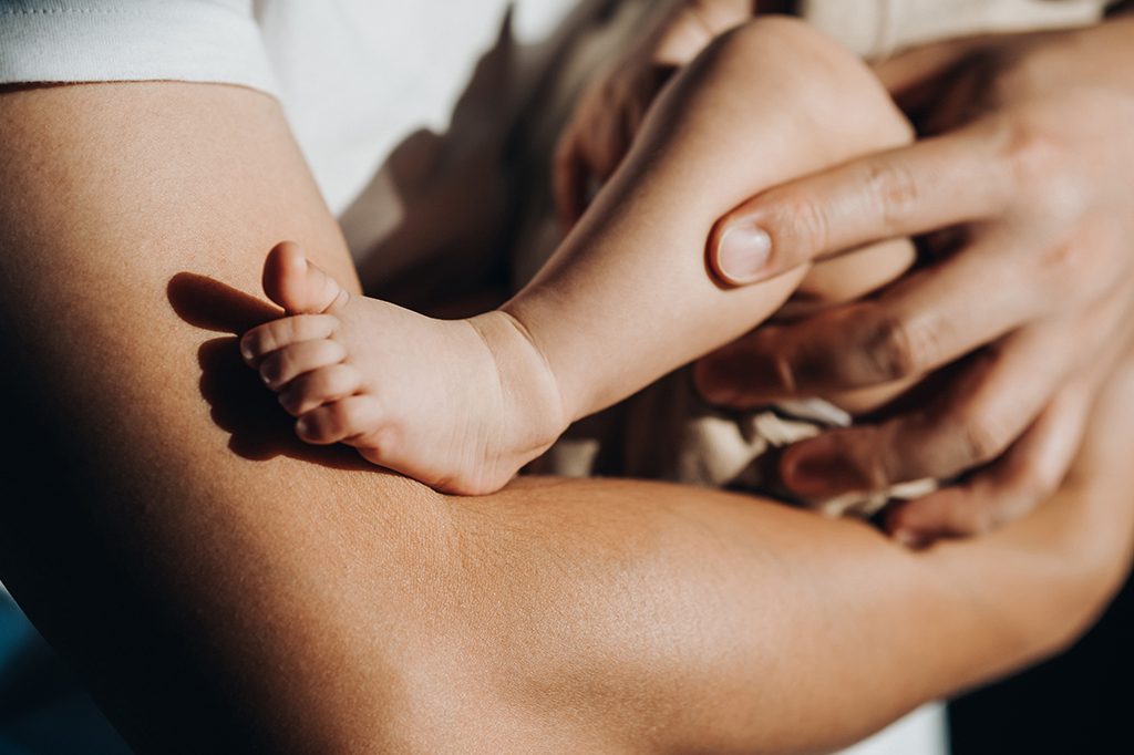 Foto de um pai carregando sua filha recém-nascida nos braços.